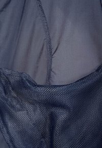 Tejido azul marino con una superficie suave y una sección de malla, con costuras visibles y diferencias en la textura de los materiales.