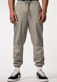 Lichtgrijze joggingsbroek met taps toelopende pijpen, een trekkoord in de taille en ribgebreide manchetten. G gedragen met zwart-witte sportsneakers.