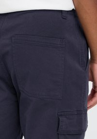 Temno modre carg kavbojke z zadnjim žepom in stranskimi carg žepi. Izdelane iz trpežnega materiala, z vidnimi šivi in gladko teksturo.