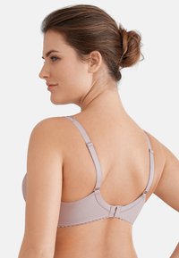 Jasnoróżowy biustonosz wykonany z gładkiego materiału, z regulowanymi ramiączkami i zapięciem na hak. Posiada falbankowe wykończenie wzdłuż pasa.