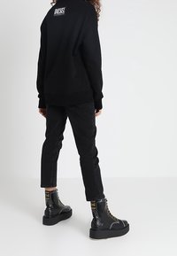 Black sweatshirt with logo on the back, paired with black jeans and black platform boots featuring gold accents and lace detailing.
