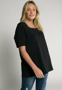T-shirt nera a maniche corte realizzata in tessuto morbido, con scollo rotondo e vestibilità ampia. Abbinata a jeans in denim blu con dettagli strappati.