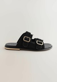 Schwarze Wildleder-Slide-Sandalen mit zwei verstellbaren Riemen und goldenen Schnallen, einer glatten schwarzen Innensohle und einer schmalen Sohle mit goldenen Akzenten.
