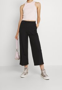 Pantalons noirs à jambes larges, crop top rose en maille, et baskets montantes à motifs. Portant un petit sac métallique rose avec une bandoulière.