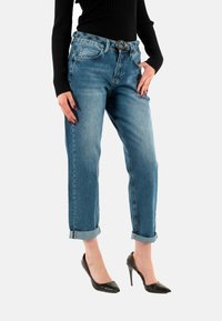 Jeans in denim azzurro chiaro con una vestibilità rilassata, orli arrotolati e una fibbia rotonda. Accompagnati da tacchi alti neri in vernice.