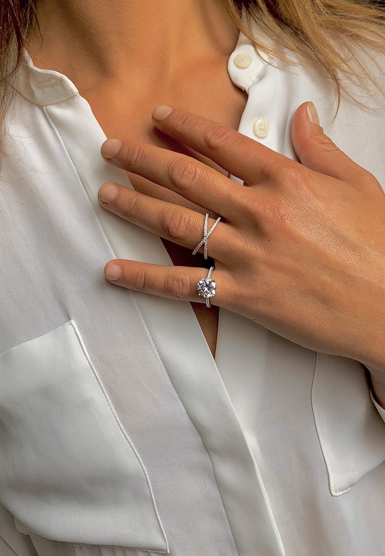 Due anelli d'argento su una mano: uno presenta una grande pietra rotonda con piccoli accenti, l'altro ha un design incrociato con piccole diamanti.