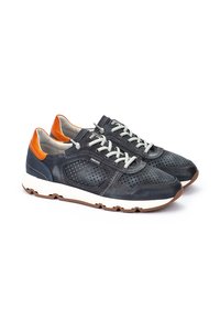 Une paire de baskets bleues marines avec des côtés perforés, des semelles blanches, des lacets gris clair et des accents orange au talon sur un fond blanc.