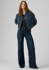 Veste en denim bleu foncé, dotée de deux poches poitrine, de boutons en argent et d'une coupe courte, assortie à un jean évasé à taille haute bleu foncé.