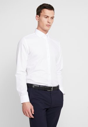 Weißes Langarm-Hemd mit Knöpfen und Kragen, kombiniert mit dunklen Hosen. Der Gürtel ist aus schwarzem Leder mit einer silbernen Schnalle. Insgesamt glatte Textur.