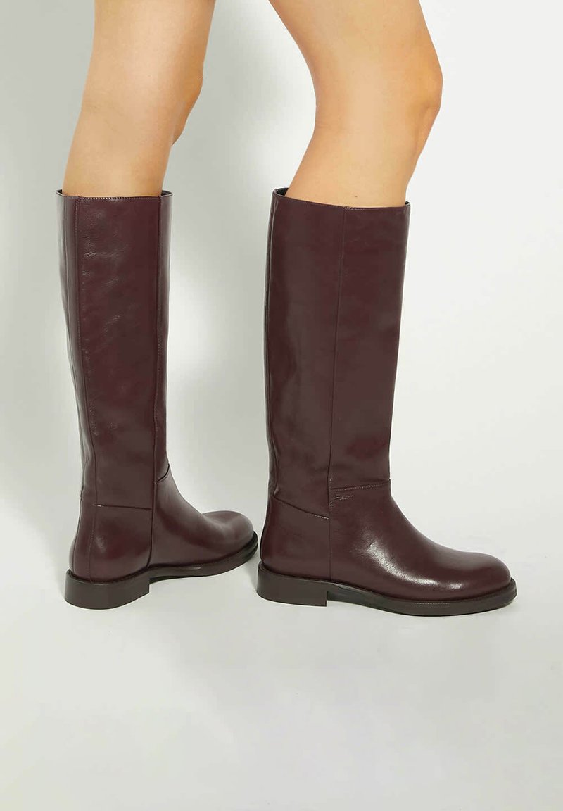 Brown leather knee-high boots with a smooth finish, minimalistic design, rounded toe, and low block heel. Side seam detailing visible.