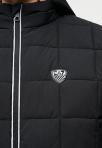 Μαύρο καπιτονέ μπουφάν με ψηλό γιακά, μπροστινό φερμουάρ και λογότυπο EA7 στο στήθος. Διαθέτει αντίθετη λευκή τρέσα κατά μήκος του φερμουάρ. Ομαλή υφή.