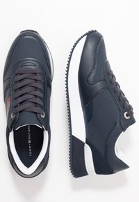 Para granatowych sneakersów Tommy Hilfiger z białymi podeszwami pośrednimi, teksturowanymi panelami i ciemnymi sznurówkami, pokazana z widoku górnego i bocznego.