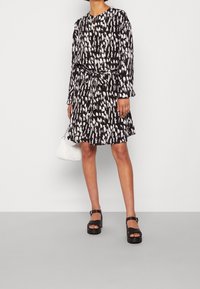 Svartvitt mönstrad klänning med långa ärmar, ett knytband i midjan och en knälång kjol. Matchad med svarta platåsandaler och en vit handväska.