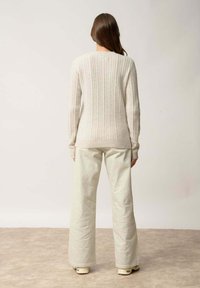 Kermakuvioinen neulepaita pitkilla hihoilla, yhdistetty vaaleanbeigeihin leveälahkeisiin housuihin. Neulepaidassa on pyöreä pääntie ja teksturoitu kangas.