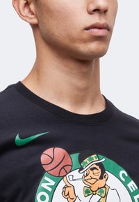 Κοντινό πλάνο ενός ατόμου που φοράει μαύρο μπλουζάκι των Boston Celtics με λογότυπο λεπτρουτσάν και πράσινο σήμα Nike στο στήθος.