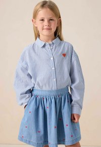 Chemise à rayures bleues et blanches avec un patch en forme de cœur, associée à une jupe en denim ornée de petits motifs en cœur rouges.