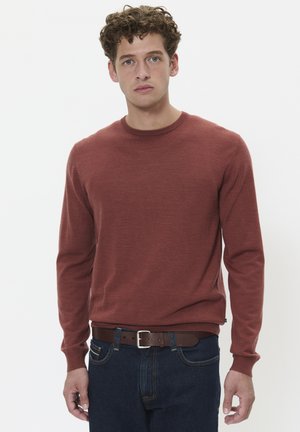 Bordeauxroter Strickpullover mit Rundhalsausschnitt, langen Ärmeln und gerippten Bündchen. Kombiniert mit dunkelblauen Jeans und einem braunen Gürtel.