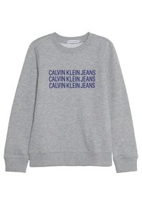 Szary sweter z długimi rękawami, ściśle dopasowanym wykończeniem rękawów i dekoltem. Posiada wyraźny niebieski napis "CALVIN KLEIN JEANS" powtórzony w trzech liniach na przodzie.