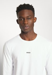 Hvid langærmet skjorte med rund halsudskæring og et lille sort "BOSS" logo på brystet. Glat tekstur med let stræk.