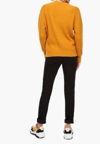 Senapsgul ribbad tröja, svarta smala jeans och chunky vita sneakers med gula detaljer. Fokusera på textur och avslappnad silhuett.