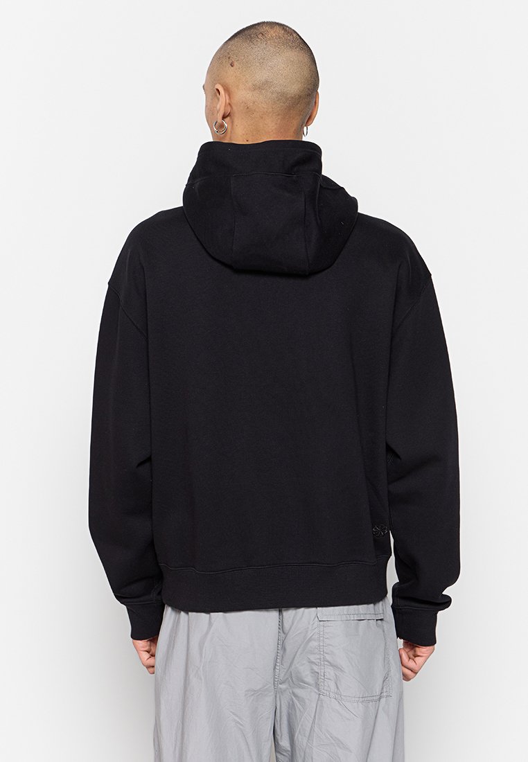 Schwarzer, übergroßer Hoodie mit einer Kordelzugkapuze und gerippten Bündchen. Weicher Stoff, mit einem subtilen Logo-Detail nahe dem Saum.