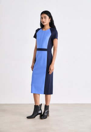 Blue and navy color-blocked dress with short sleeves, a fitted silhouette, and a knee-length hem. Worn with black ankle boots.