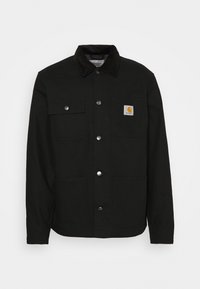 Giacca nera Carhartt con colletto in corduroy, quattro tasche frontali e bottoni a pressione argentati, patch del logo sulla tasca superiore sinistra.