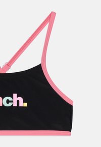 Haut de sport noir avec des bretelles et des finitions roses, mettant en avant un design de texte coloré "inch." en teintes pastel. Texture de tissu lisse.