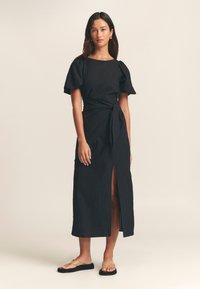Czarna sukienka maxi z krótkimi bufkami rękawów, talią z paskiem i bocznym rozcięciem. Wykonana z teksturowanej tkaniny, charakteryzująca się czystym, minimalistycznym designem.