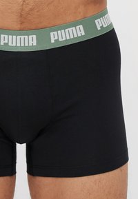 Black cotton boxer briefs with a light green waistband featuring "PUMA" printed in white. Smooth texture and fitted design.