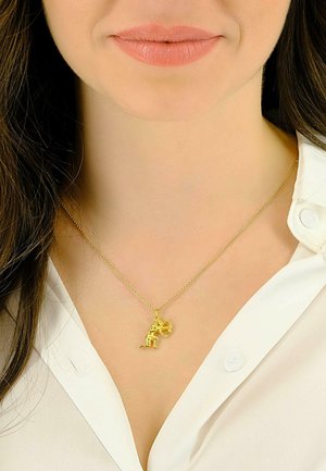 Collier en or avec un pendentif détaillé représentant une figure tenant un objet circulaire, sur une blouse blanche. La chaîne est fine et texturée.