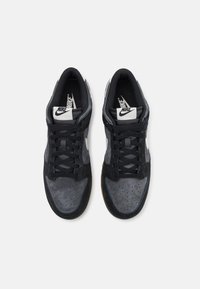 Ténis pretos e cinzas com painéis de camurça e malha, atacadores planos, caixa do dedo perfurada e sola de borracha de goma. Logótipo da Nike na língua.