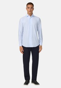 Lichtblauw overhemd met verticale witte strepen, lange mouwen, puntige kraag, ingestopt in donkerblauwe broek en gecombineerd met zwarte sneakers.