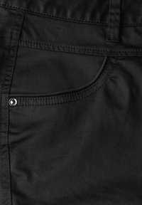 Pantalon en coton noir avec une poche avant ornée de détails de couture et d'un bouton en métal brillant. Texture lisse avec des éléments de design minimaux.