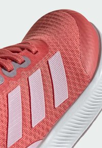 Różowy but sportowy z cholewką z teksturowanej tkaniny, trzema jasnoróżowymi paskami i białą, karbowaną gumową podeszwą.