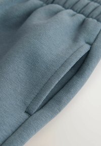 Blue cotton joggers with a textured surface, featuring an elastic waistband and a side pocket. The fabric is soft and slightly stretchy.