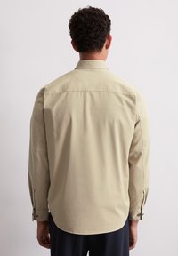 Lichtbeige button-up shirt met lange mouwen, een achterpand, afgeronde zoom en details bij de manchetten. De stof lijkt glad en heeft een ontspannen pasvorm.