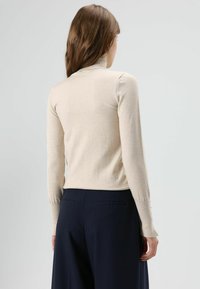 Pull beige à col roulé avec manches longues, poignets côtelés et texture lisse. Associé à un pantalon large taille haute bleu marine foncé.