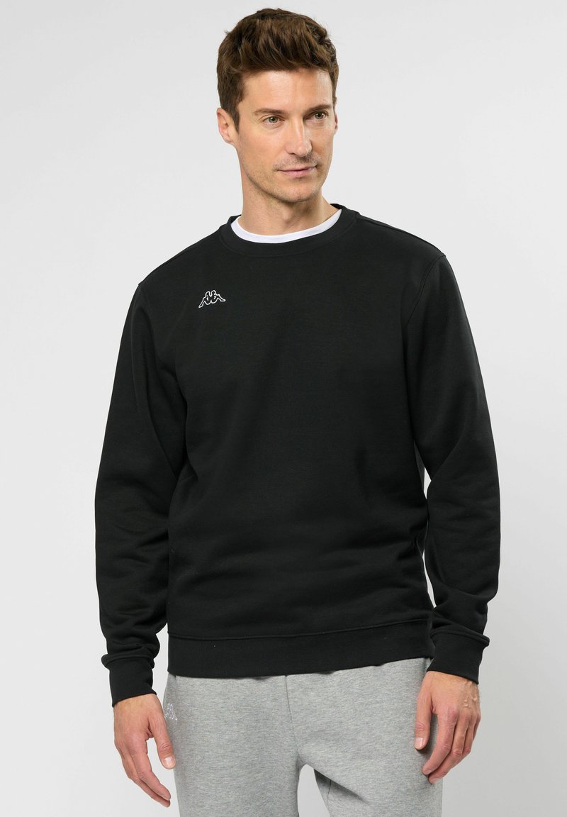 Svart sweatshirt med långa ärmar, ribbad rund halsringning och en liten vit logotyp på vänster bröst. Tillverkad av bomull, avslappnad passform, texturerat tyg.