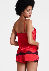 Ensemble en satin rouge comprenant un débardeur et un short, avec une délicate bordure en dentelle noire. Bretelles ajustables, texture lisse et ourlet évasé.
