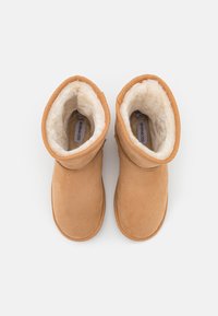 Paire de bottes d'hiver en daim beige avec doublure blanche et duveteuse, vues de dessus sur un fond blanc.