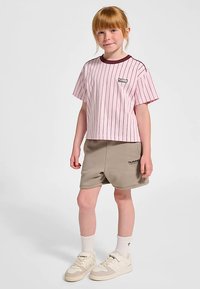 Rosa randig t-shirt med kort ärm och mörk kant, kombinerad med beige shorts. Sneakers är vita med ljusbruna detaljer. Strumporna är vita.