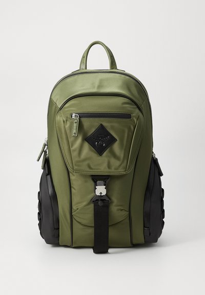 Mochila verde oliva con un acabado de satén suave, que presenta un bolsillo delantero con cremallera, detalles en negro y un panel lateral texturizado. Correas ajustables.
