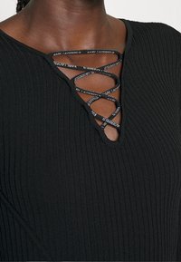 Schwarzes, geripptes Top mit V-Ausschnitt und gekreuzten Spitze-Details sowie markierten Trägern. Glatte Textur mit enganliegender Silhouette.