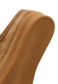 Close-up van een bruine suède schoenenzool met een gestructureerde rubberen buitenzool en zichtbare stiksels langs de rand.