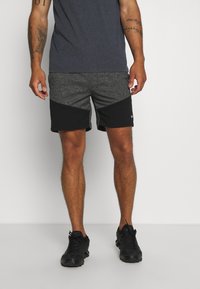 Zwarte en grijze sportshorts met een textuurdesign, met een kleurblokpatroon en een klein logo-detail op de heup. G gedragen met zwarte sneakers.