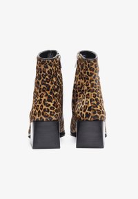 Bottes cheville en imprimé léopard avec une finition en daim texturé, un talon carré noir et une fermeture éclair latérale pour un enfilage facile.