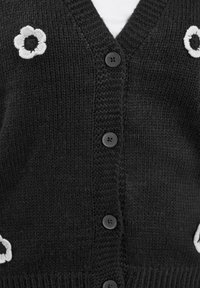Czarny dziergany kardigan z dekoltem w serek, ozdobiony białym haftem kwiatowym i sześcioma czarnymi guzikami z przodu. Subtelna tekstura prążkowana.
