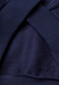 Sudadera navy de tela con puños y dobladillo acanalados. El interior tiene una textura suave y cepillada. Incluye costura superior a lo largo del dobladillo y las costuras.