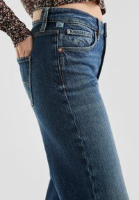 Dunkelblaue Jeans aus Denim mit geradem Schnitt, ausgestattet mit Kupferriegeln, Vordertaschen und einem gestickten Logoetikett am Bund.